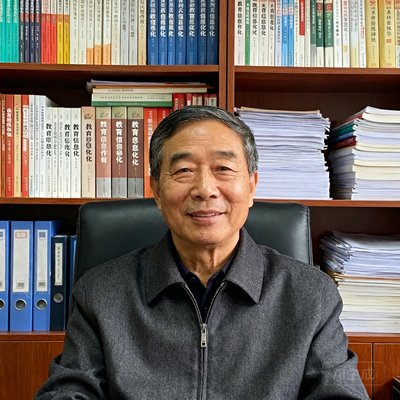 贵州黔东南州教育局电教馆刘明远主任的肖像照，他大约50岁，穿着深灰色夹克，坐在办公室中，背后的书架上整齐排列着教育信息化相关的书籍和文件